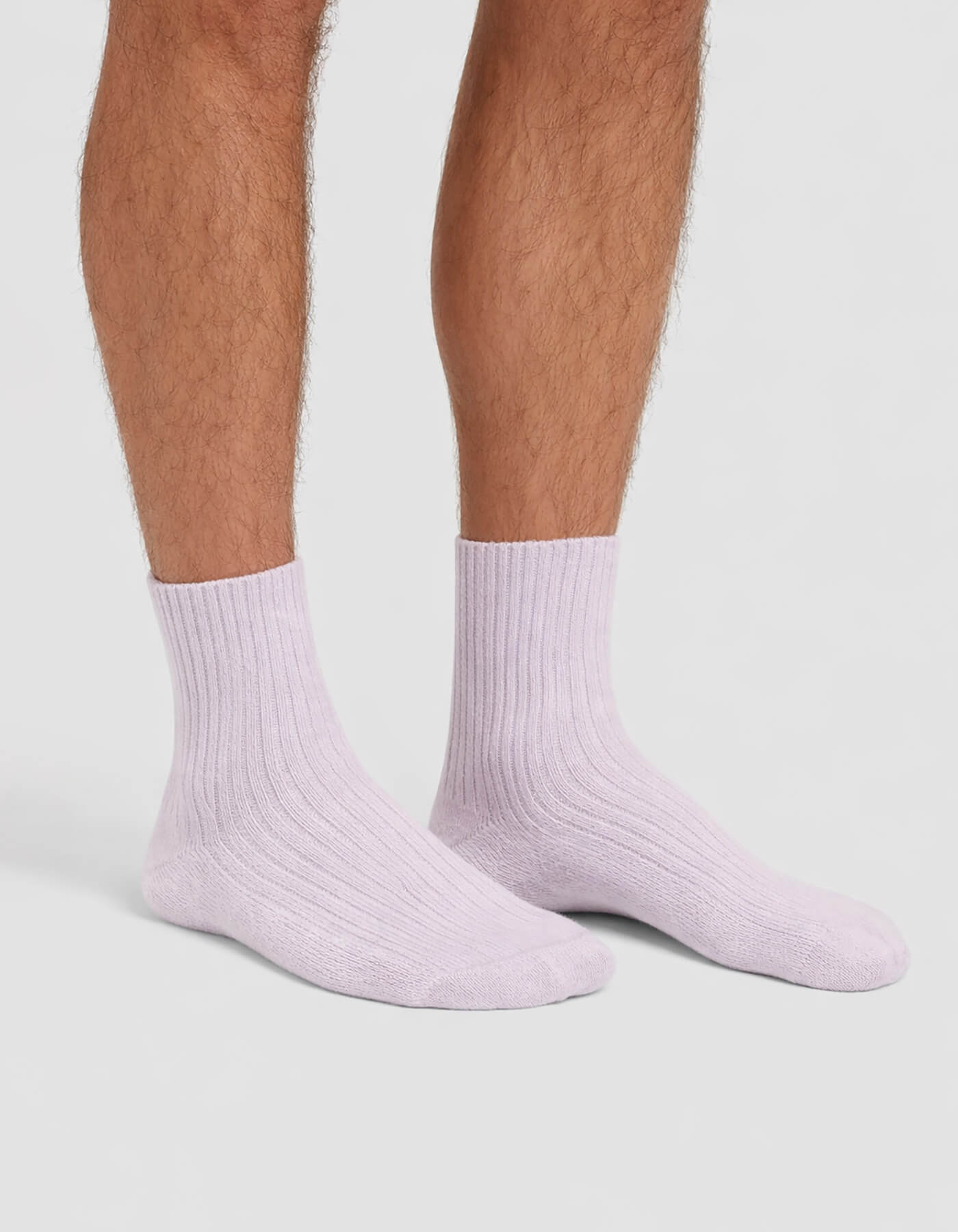 A person with light brown, hairy legs is wearing Cozy Earth Men's Plush Lounge Crew Socks in light purple, standing on a plain white background.
