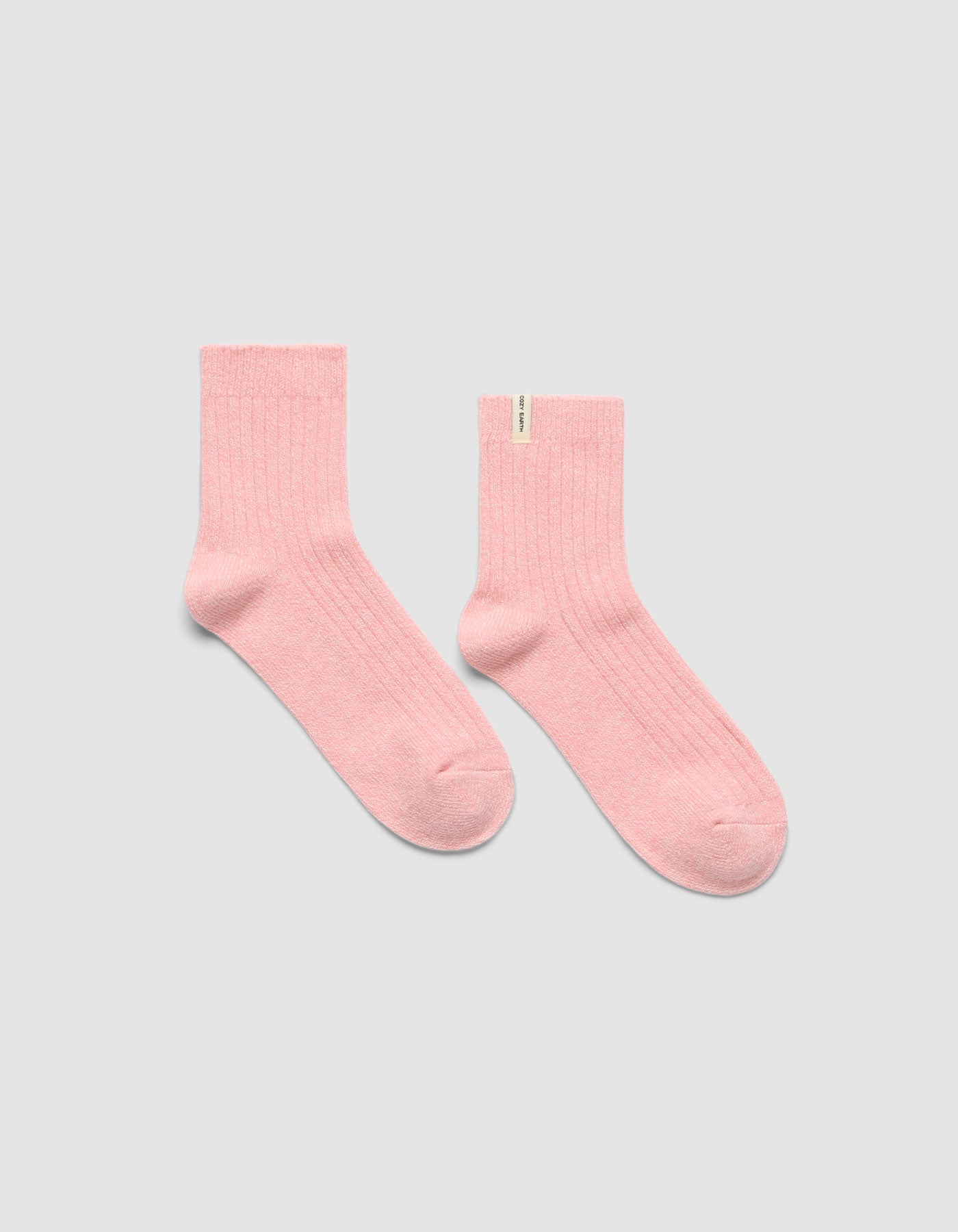 A pair of light pink The Plush Modern Crew Socks by Cozy Earth is laid flat on a plain light gray background, with one sock featuring a small white tag near the top.