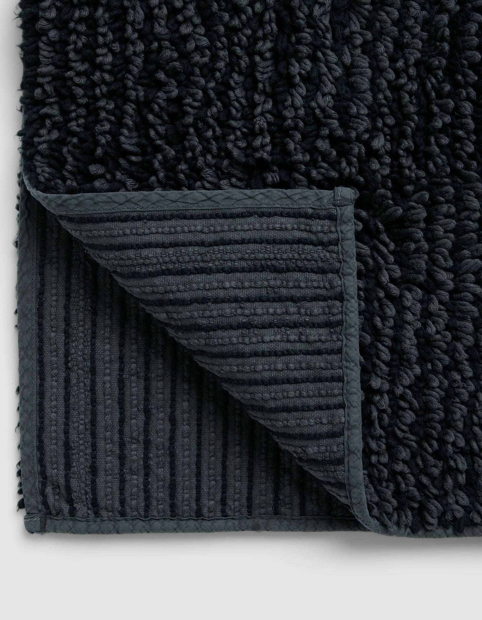 Close-up of the Cozy Earth Plush Loop Bath Mat with a corner folded, highlighting its ribbed, non-slip underside and thick, soft plush pile on top.