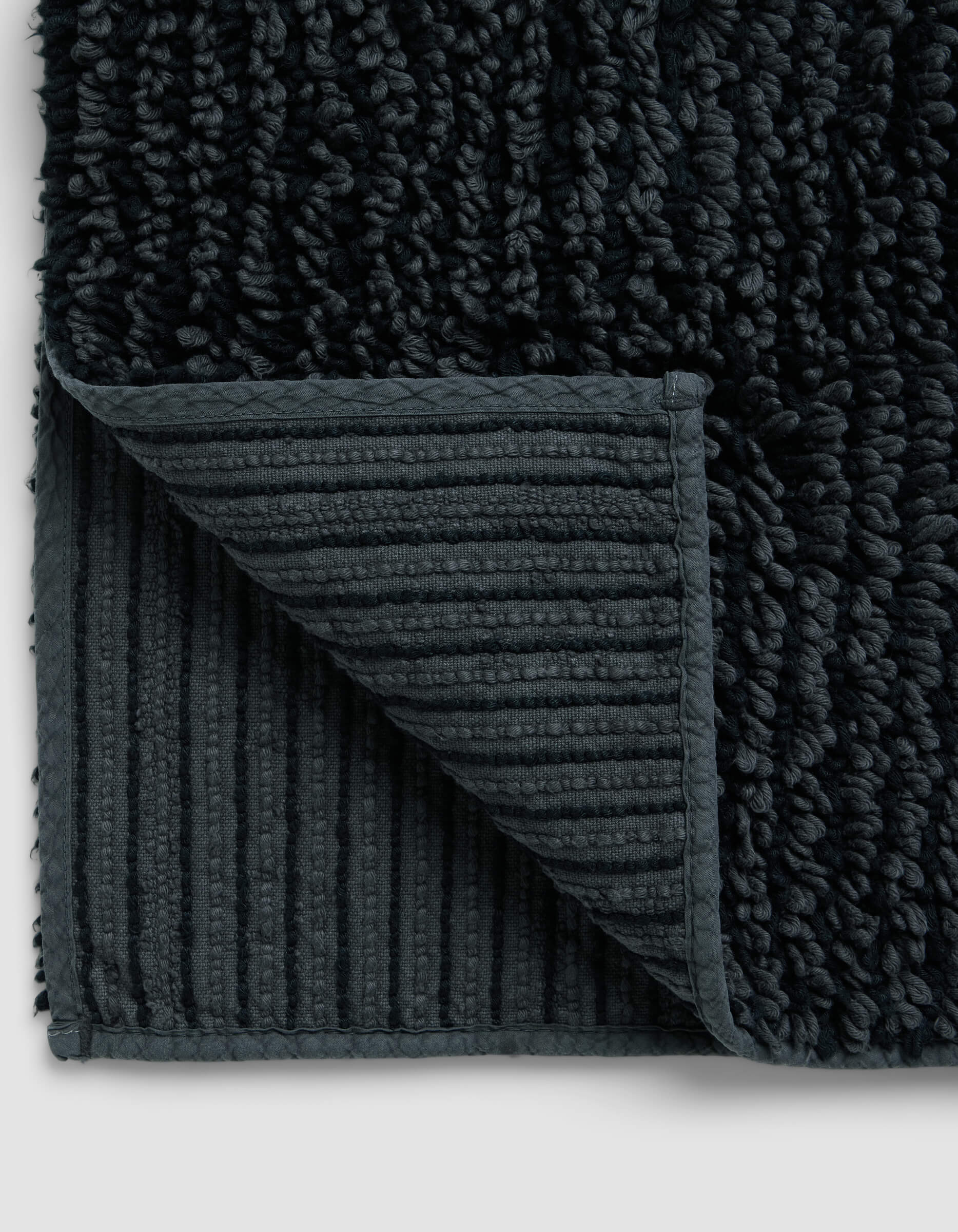 Close-up of the Cozy Earth Plush Loop Bath Mat with a corner folded, highlighting its ribbed, non-slip underside and thick, soft plush pile on top.