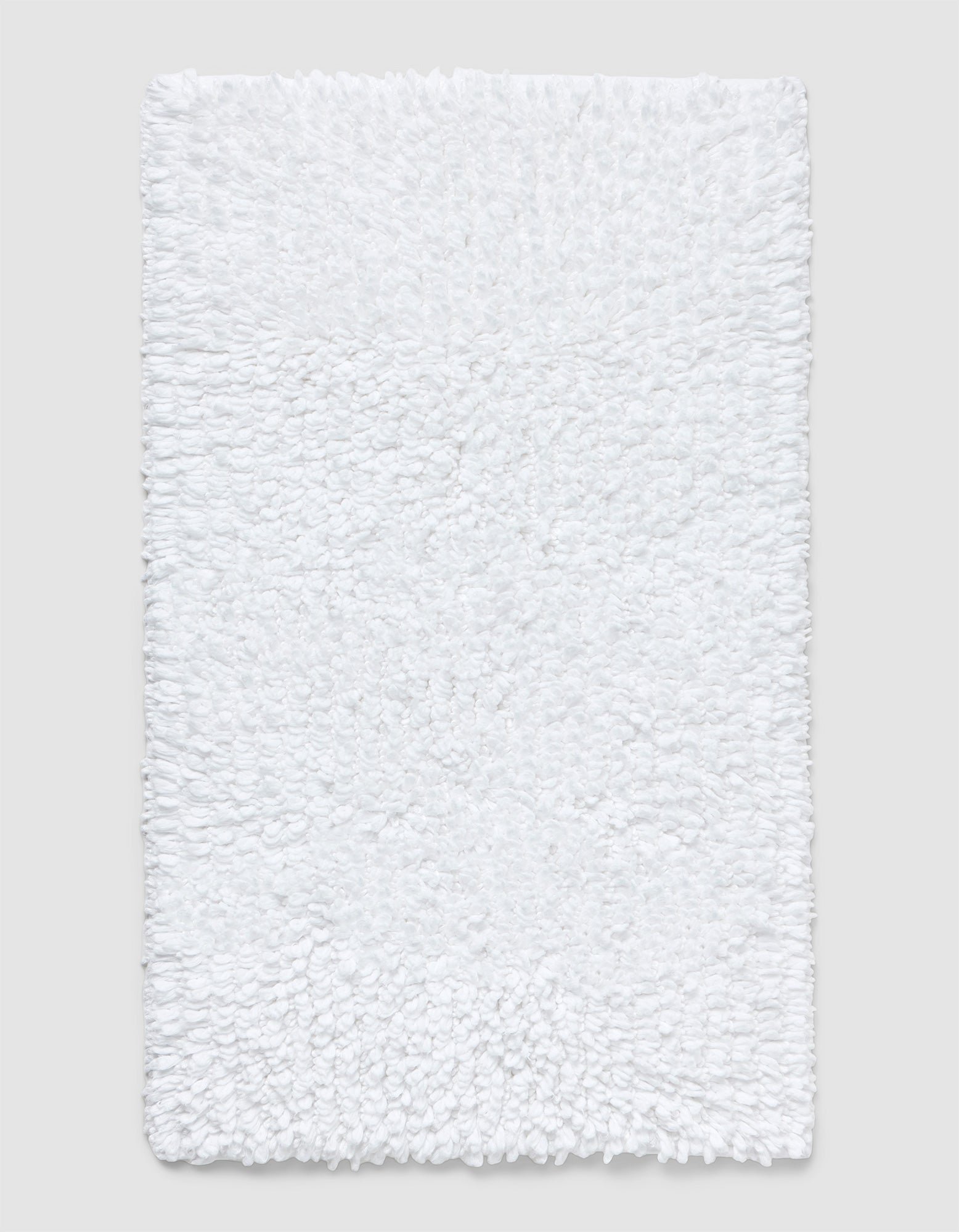 The Cozy Earth Plush Loop Bath Mat is rectangular, white, and features a soft, fluffy chenille shag texture. Shown on a plain light background, it offers plush comfort with its textured surface.