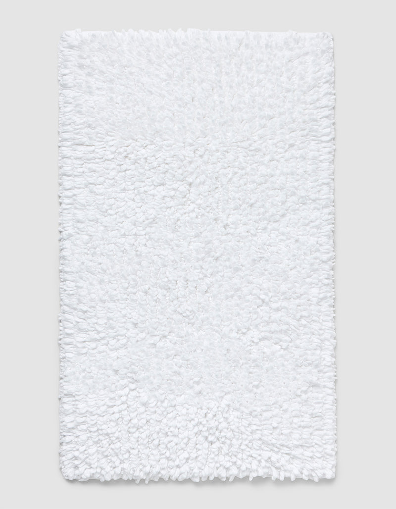 The Cozy Earth Plush Loop Bath Mat is rectangular, white, and features a soft, fluffy chenille shag texture. Shown on a plain light background, it offers plush comfort with its textured surface.
