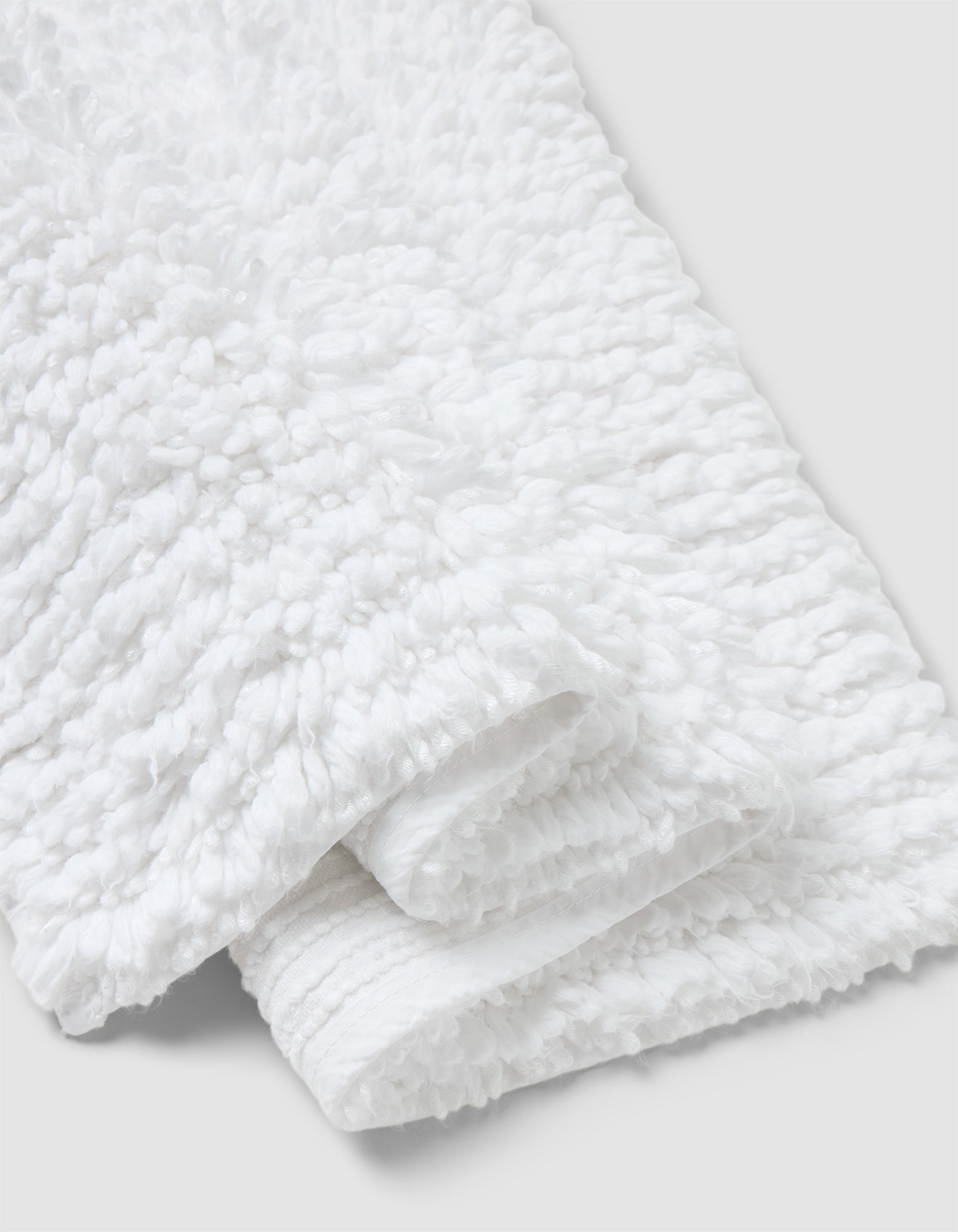 A close-up of the Cozy Earth Plush Loop Bath Mat, folded on a light gray background. The mat’s fluffy, looped texture highlights its softness and absorbency.