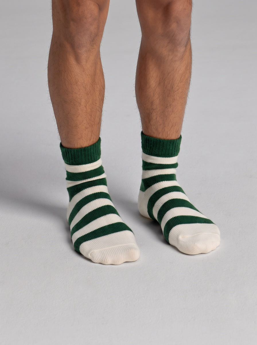 A person wearing Cozy Earth Women’s Plush Lounge Quarter Socks with wide green and white horizontal stripes and plain white toes.
