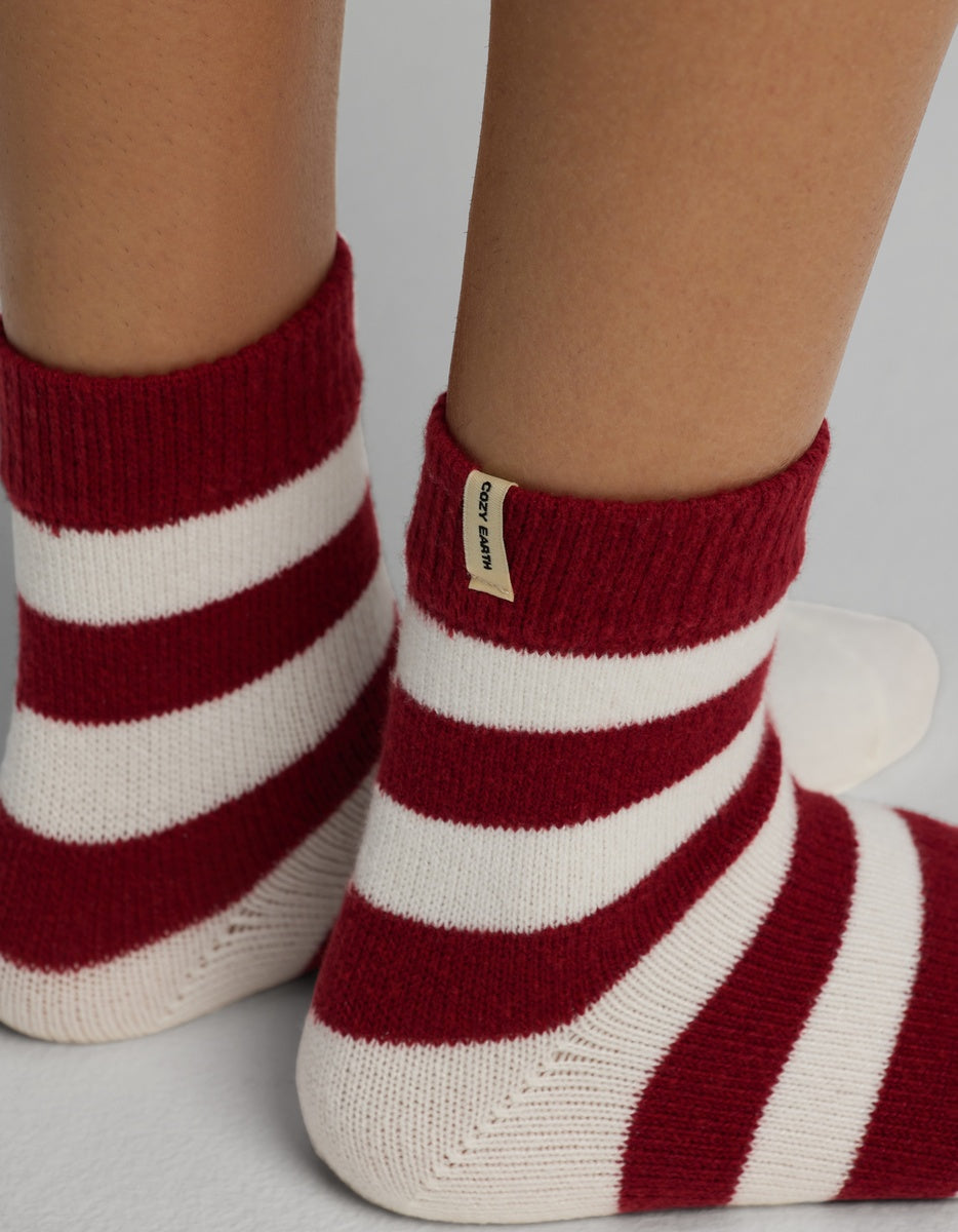 Feet wearing red and white striped Women’s Plush Lounge Quarter Sock ankle socks with a small branded tag on the cuff.