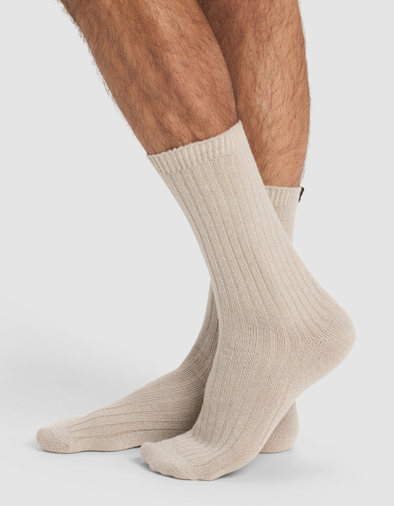 A close-up of a person wearing Cozy Earth’s The Plush Lounge Calf Sock 3-Pack in cream, standing with one foot slightly ahead of the other against a plain white background.