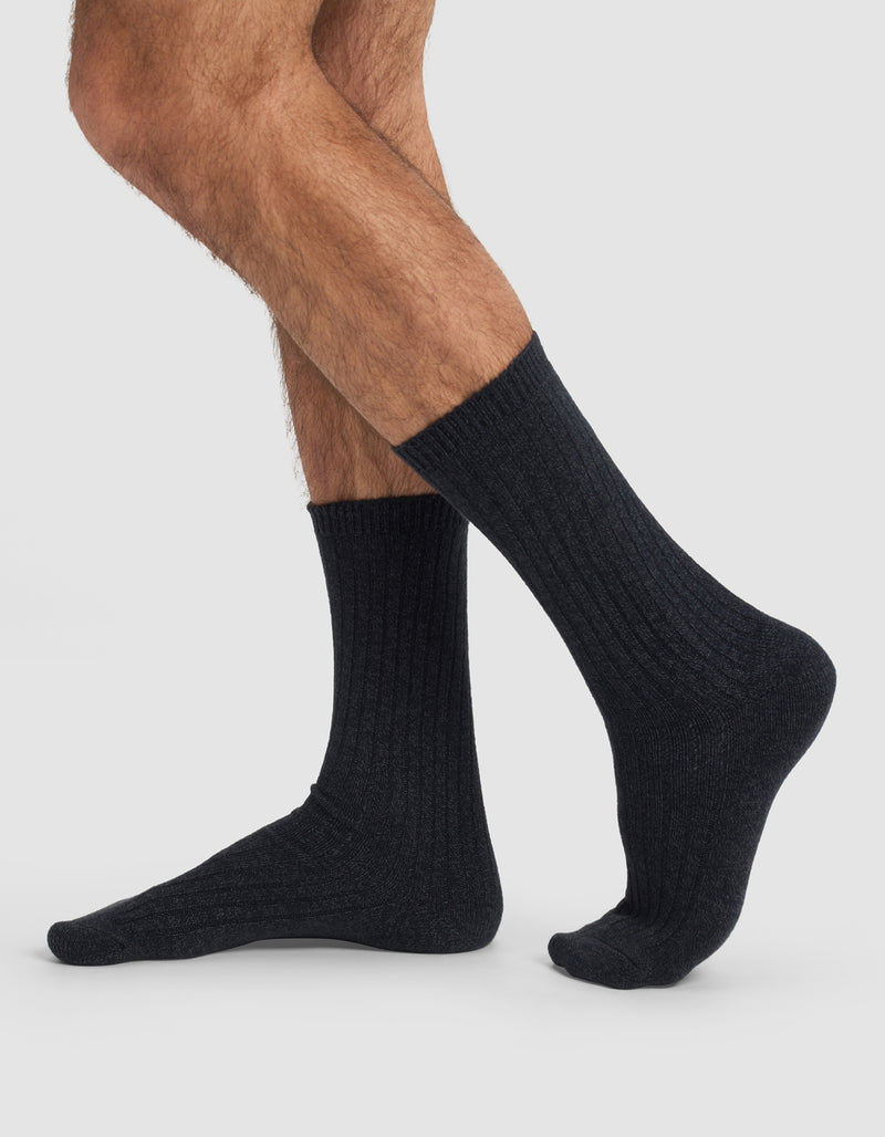 A person with crossed legs wears Cozy Earth's The Plush Lounge Calf Sock 3-Pack, dark ribbed crew socks, photographed from the side against a plain light background.