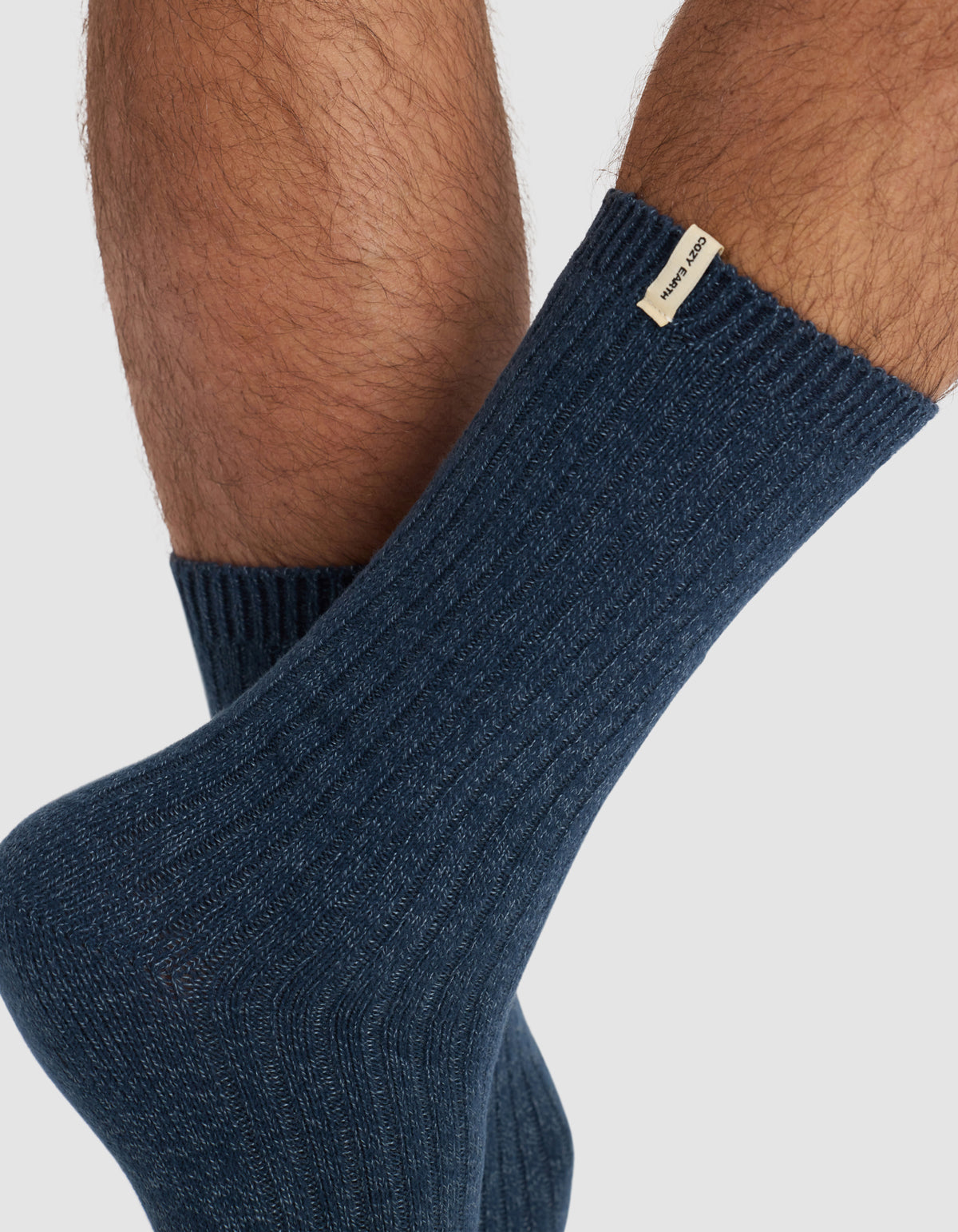 Close-up of a person’s lower legs wearing Cozy Earth's The Plush Lounge Sock 3-Pack in ribbed dark blue, featuring a small beige label near the top, set against a plain light background.