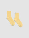The Plush Modern Crew Sock by Cozy Earth in light yellow, featuring a ribbed crew design, is displayed laid flat on a light gray background.|Color:Daisy