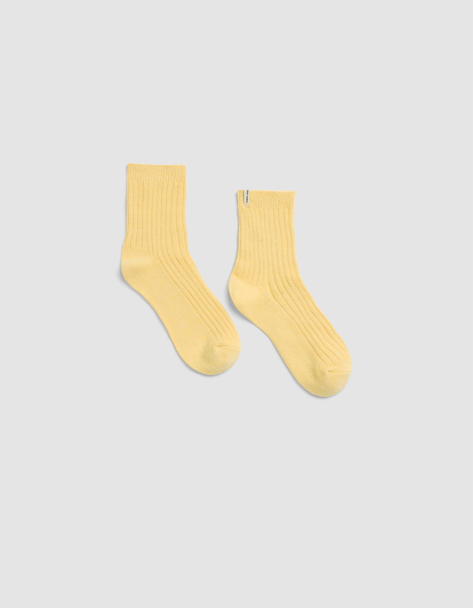 The Plush Modern Crew Sock by Cozy Earth in light yellow, featuring a ribbed crew design, is displayed laid flat on a light gray background.