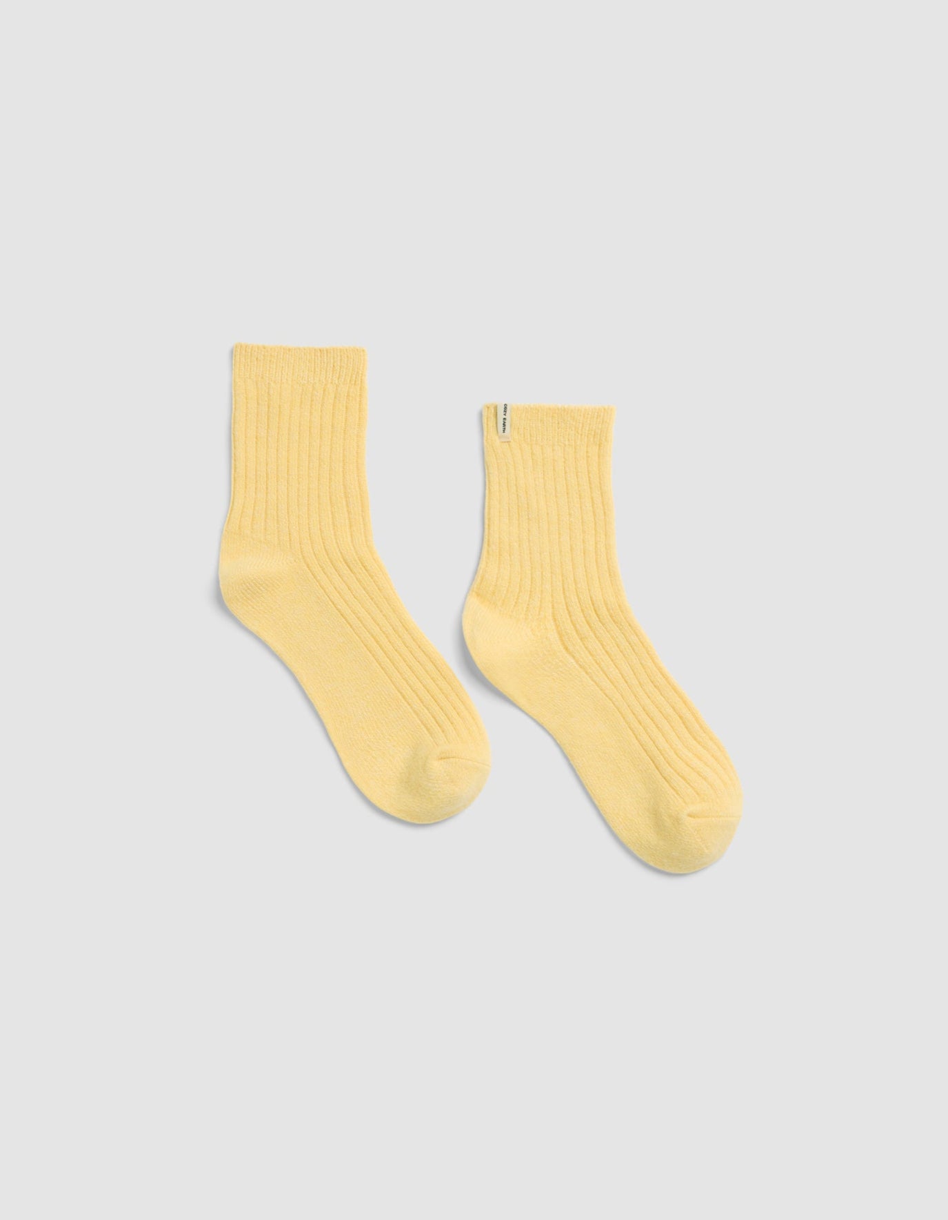 The Plush Lounge Quarter Socks by Cozy Earth in light yellow, featuring a ribbed crew design, is displayed laid flat on a light gray background.