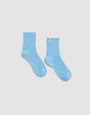 The Plush Modern Crew Sock by Cozy Earth in light blue features a ribbed design and a small yellow tag on the upper edge, shown against a plain white background.|Color:Harbor