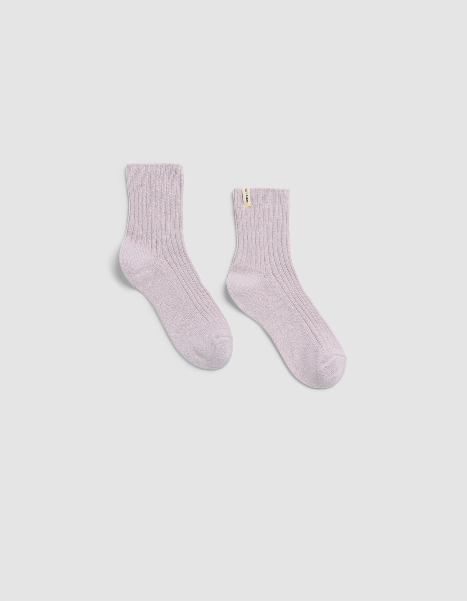 The Plush Modern Crew Sock by Cozy Earth in light pink features a ribbed design and a small yellow tag on one sock, shown against a plain white background.