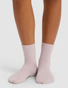 A person wears Cozy Earth’s The Plush Modern Crew Sock in light pink, featuring a ribbed design, standing on a white surface with only their lower legs and feet visible.|Color:Lavender