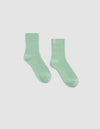A pair of The Plush Modern Crew Socks by Cozy Earth, in light green ribbed fabric, is laid flat on a plain white background with one sock slightly angled outward.|Color:Wintergreen