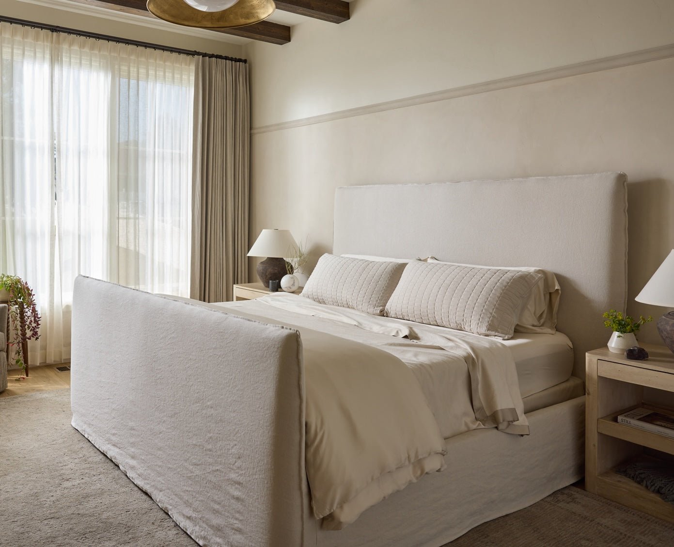 Neatly made bed in a bedroom with light-colored walls and curtains.