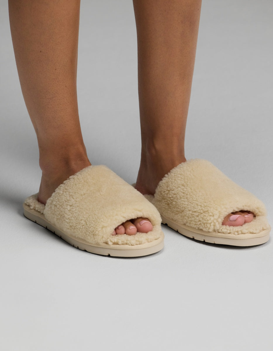 A person wearing Cozy Earth Puffy Sheep Slides stands on a light gray surface.