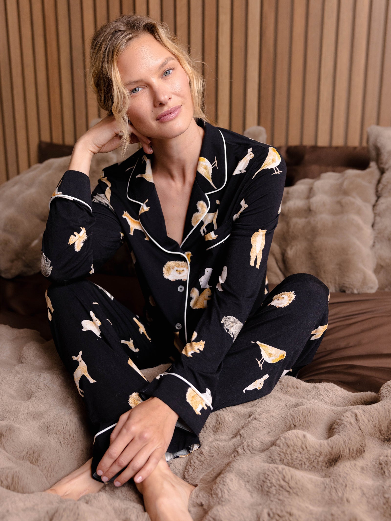 Woman sitting on a bed wearing Women's Stretch-Knit Bamboo Pajama Pant in Woodland Creatures Black 