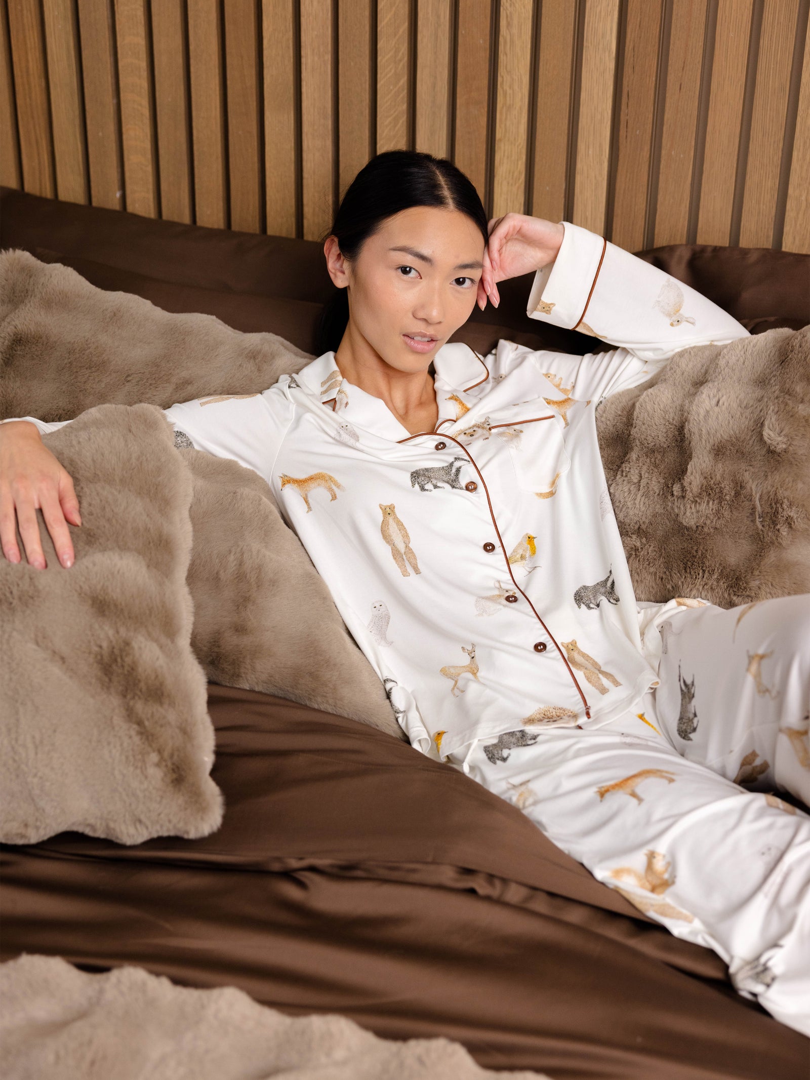 Woman lounges on a bed wearing Women's Long Sleeve Bamboo Pajama Top in Stretch-Knit - Woodland Creatures Ivor 