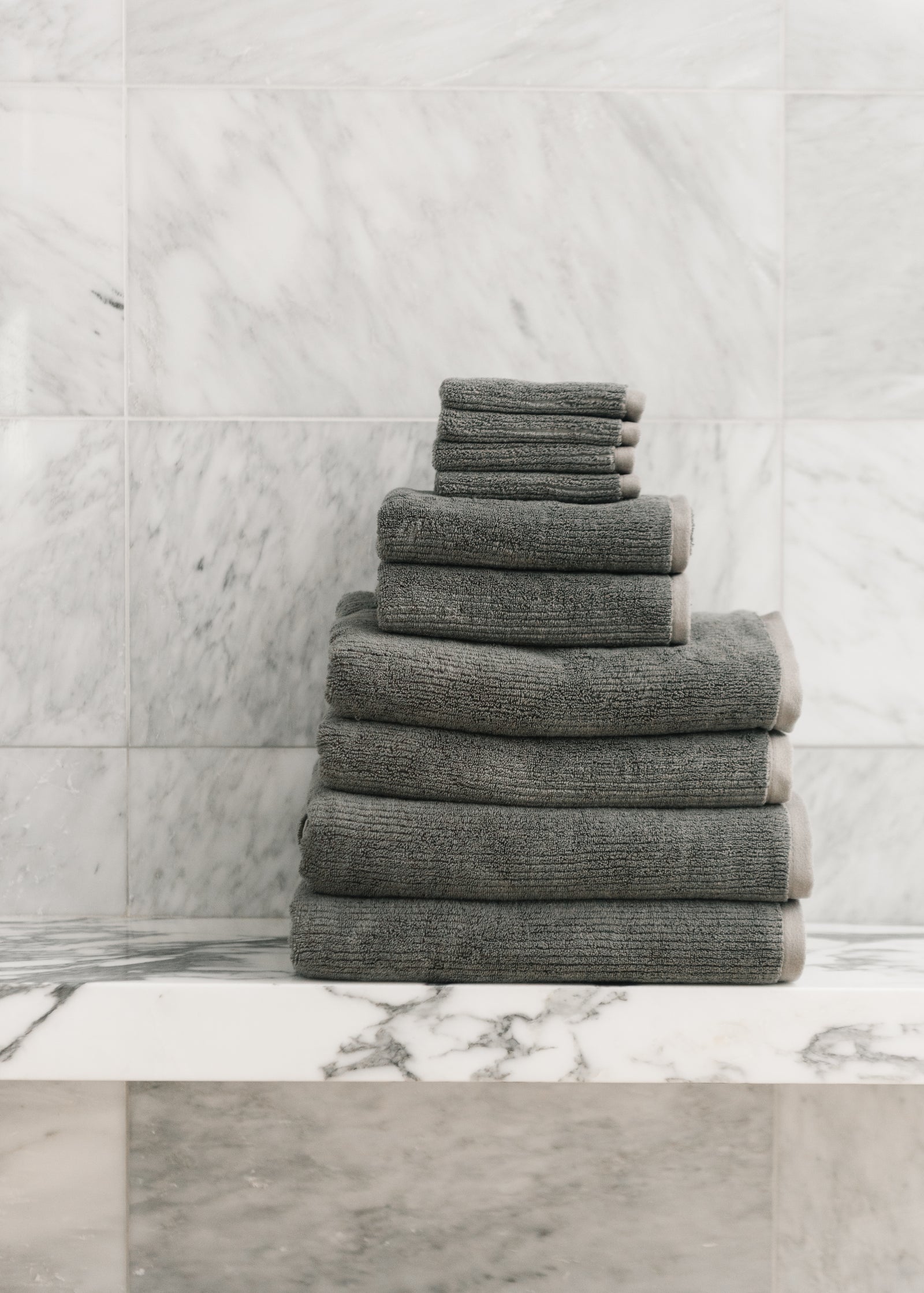 Complete Ribbed Terry Bath Bundle in the color Charcoal. Photo of Complete Ribbed Terry Bath Bundle taken in a marble bathroom. The Complete Ribbed Terry Bath Bundle are resting on a marble counter top. 