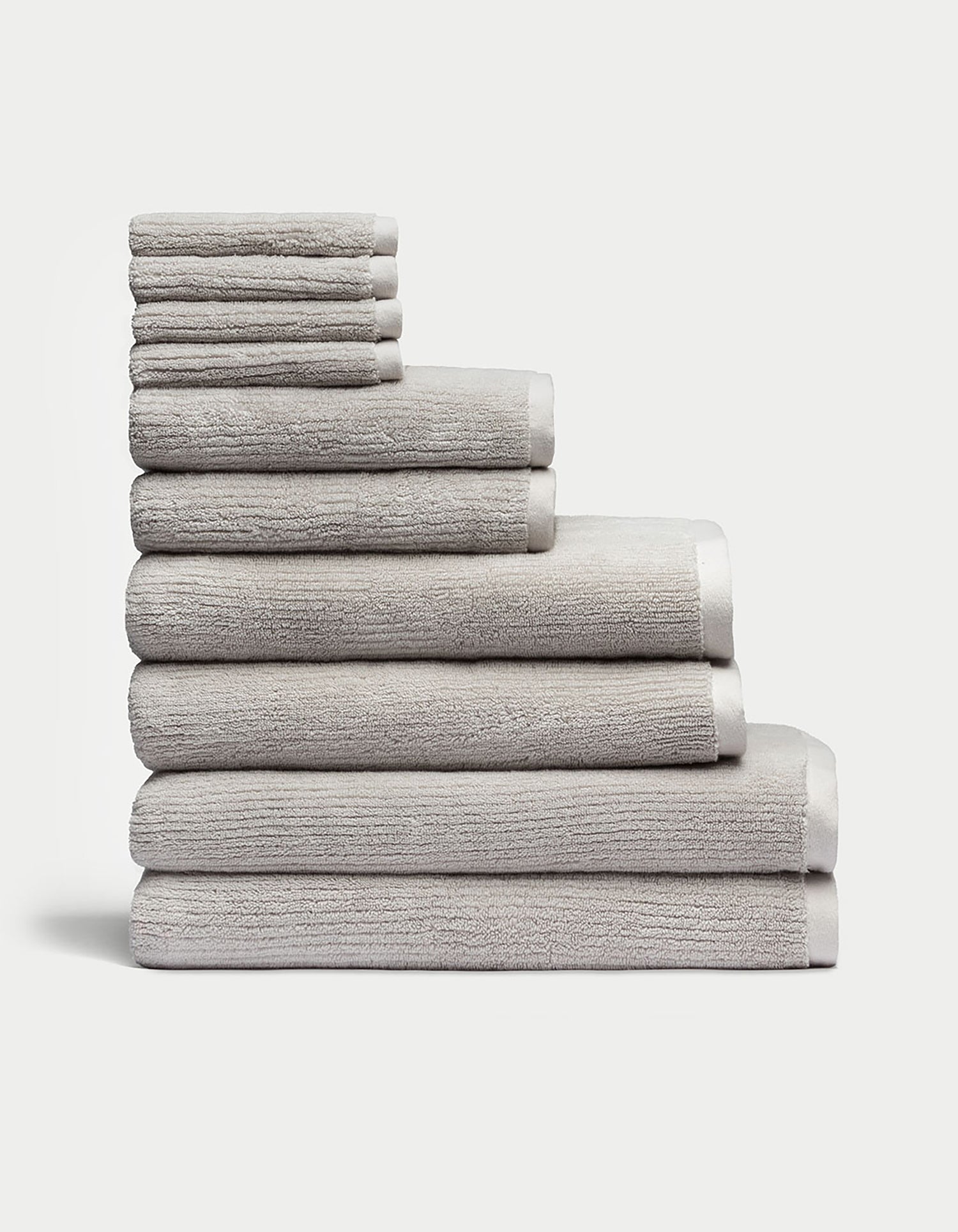 The Complete Ribbed Terry Bath Bundle by Cozy Earth features a neatly stacked arrangement of plush, gray towels in various sizes, piled eight layers high against a plain white background, showcasing their soft and textured surface for ultimate comfort.