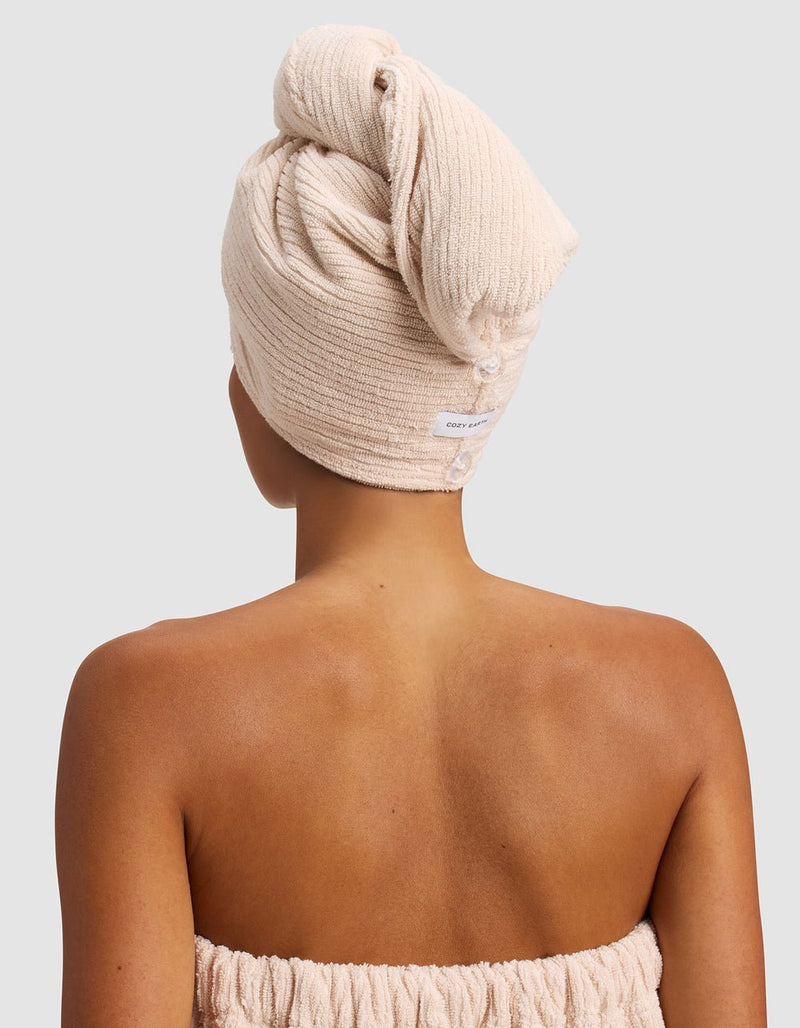 A person with medium brown skin, seen from behind, wears the Cozy Earth Ribbed Terry Hair Towel and a matching strapless towel wrap against a plain light background.