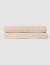 Two neatly folded beige towels from Cozy Earth's Complete Ribbed Terry Bath Bundle are stacked on top of each other against a plain light gray background.|Color:Petal