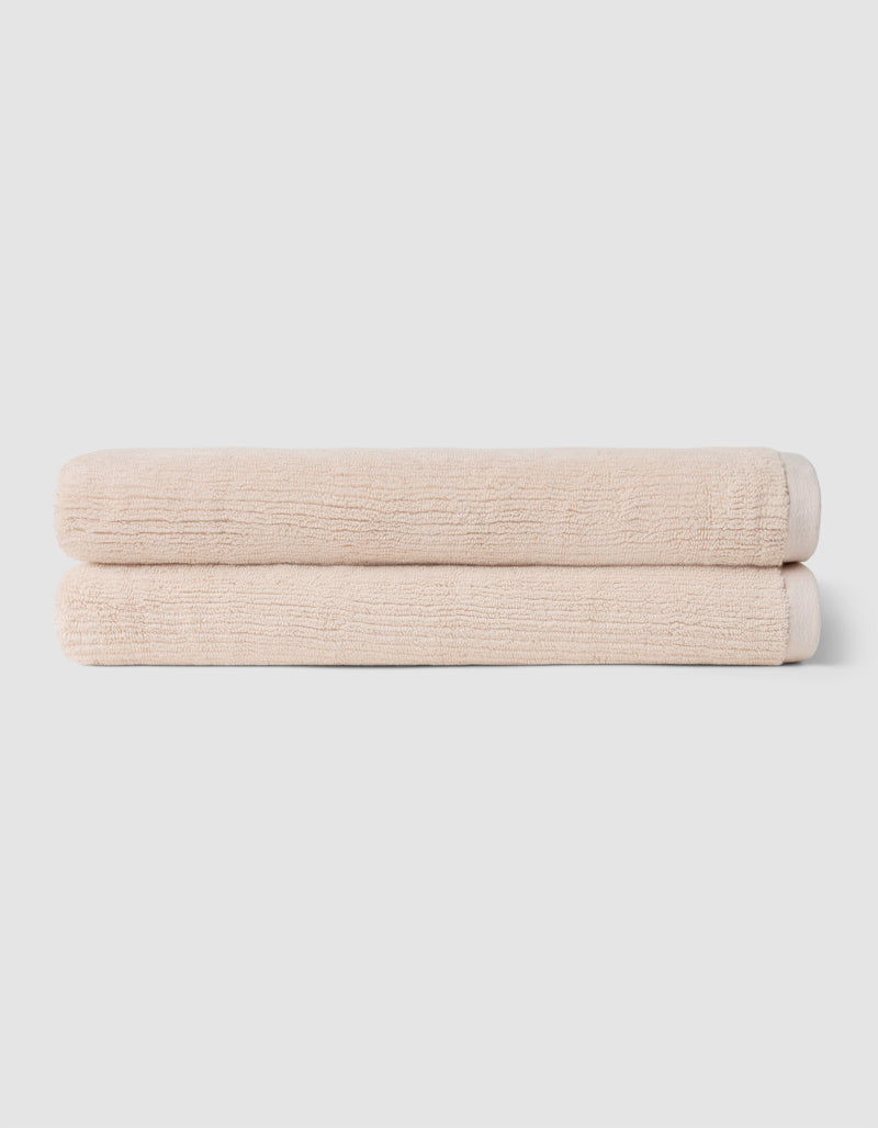 Two neatly folded beige towels from Cozy Earth's Complete Ribbed Terry Bath Bundle are stacked on top of each other against a plain light gray background.
