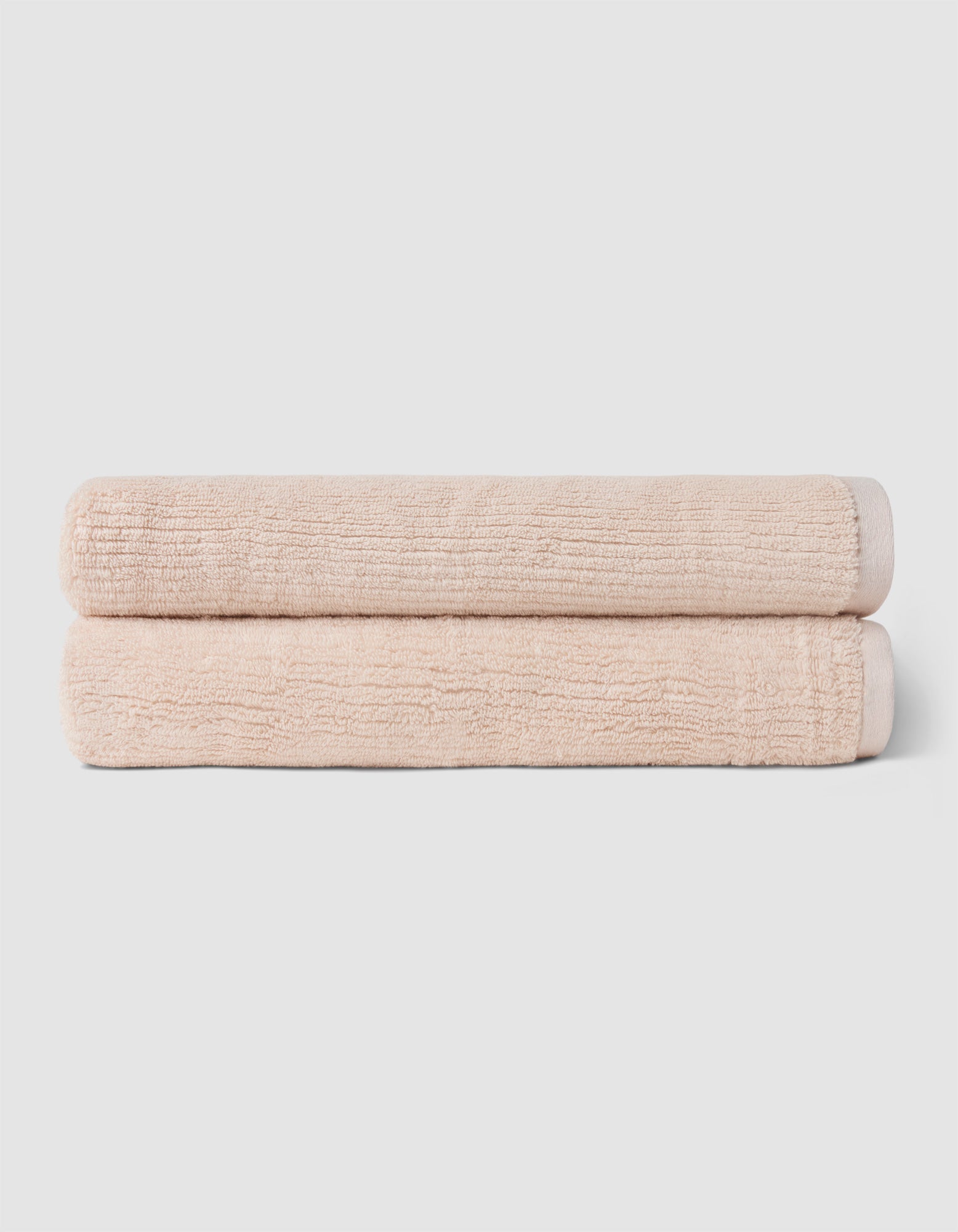 The Complete Ribbed Terry Bath Bundle by Cozy Earth features two neatly rolled, light beige towels stacked on a plain, light gray background.