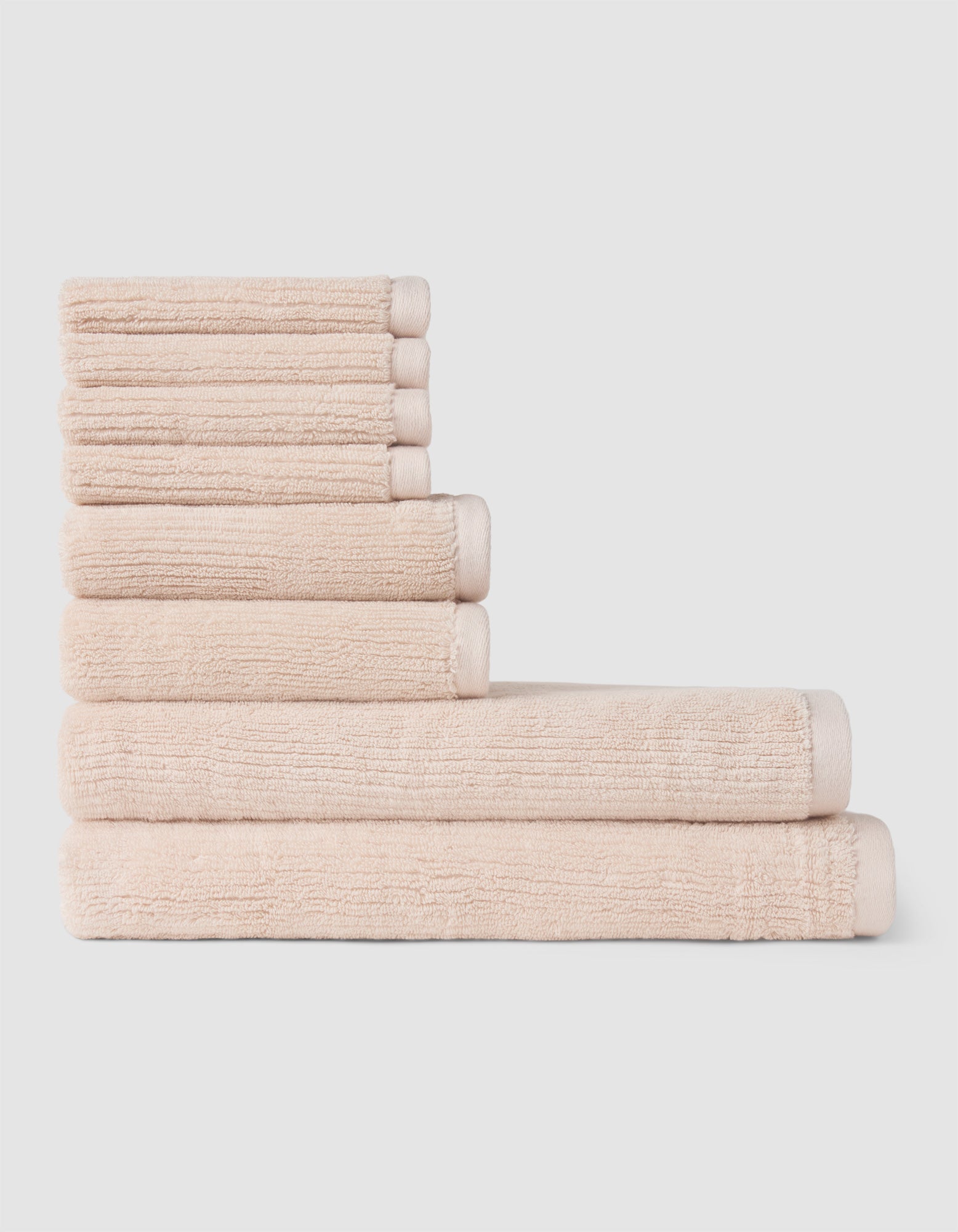 The Cozy Earth Ribbed Terry Bath Towel Set features six beige towels of various sizes, neatly stacked in a stepped formation against a plain light background.