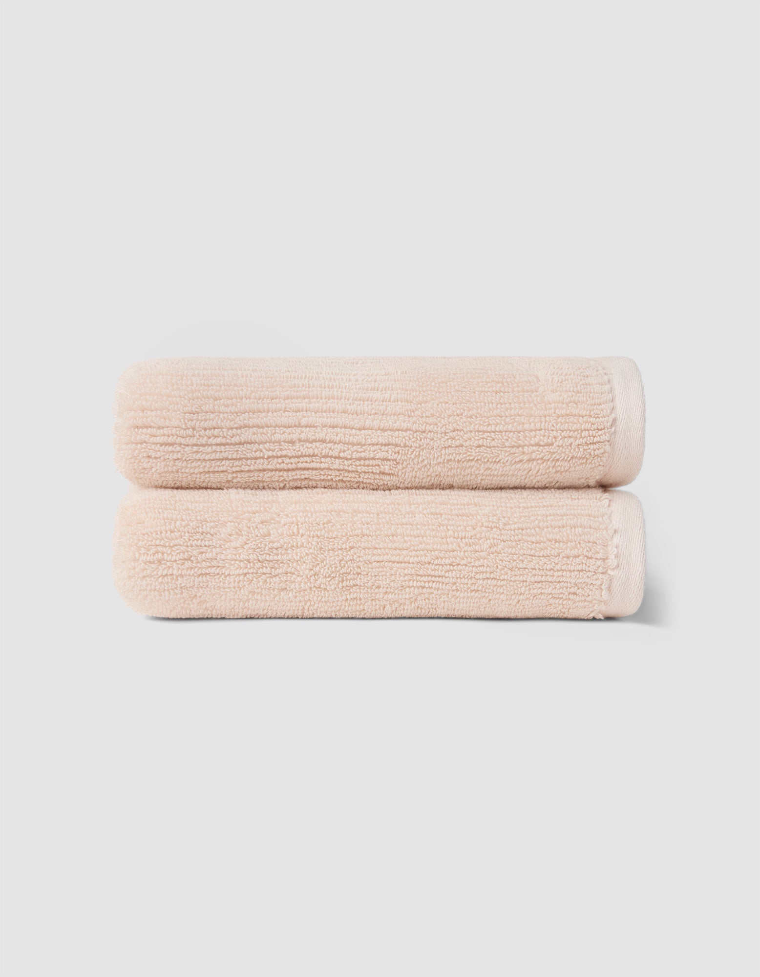 The Cozy Earth Complete Ribbed Terry Bath Bundle features two neatly folded, light beige towels stacked atop each other against a plain, light gray background.