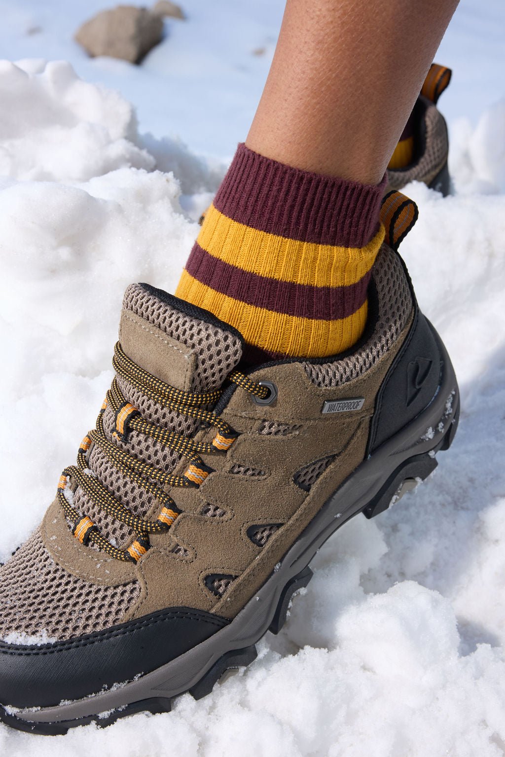 A person wearing Cozy Earth's Women's Sadie Sock in burgundy with two yellow ankle stripes, standing in snow wearing hiking boots