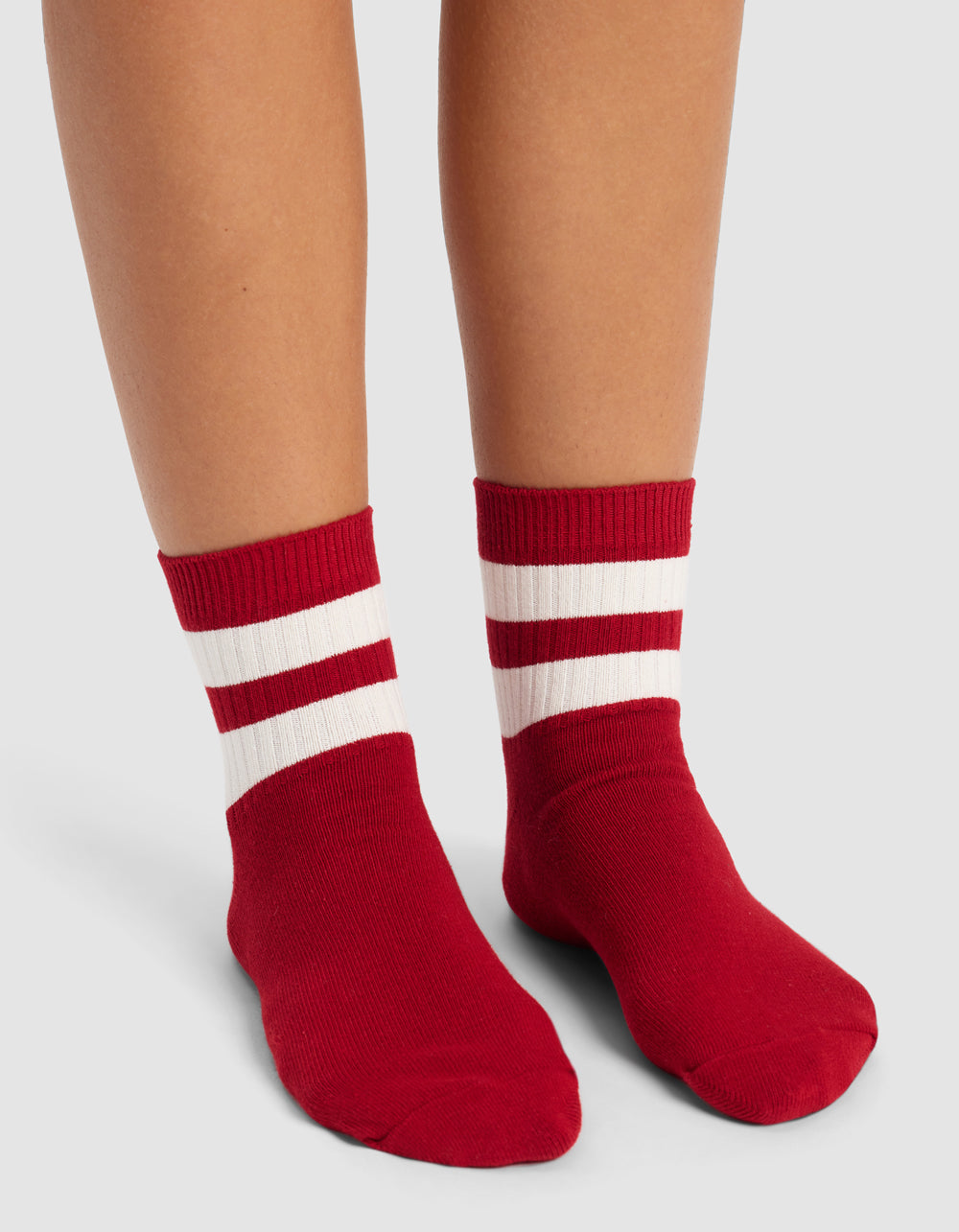 A person wearing Cozy Earth Women's Sadie Socks—red with two white horizontal stripes near the top—stands on a light gray surface.