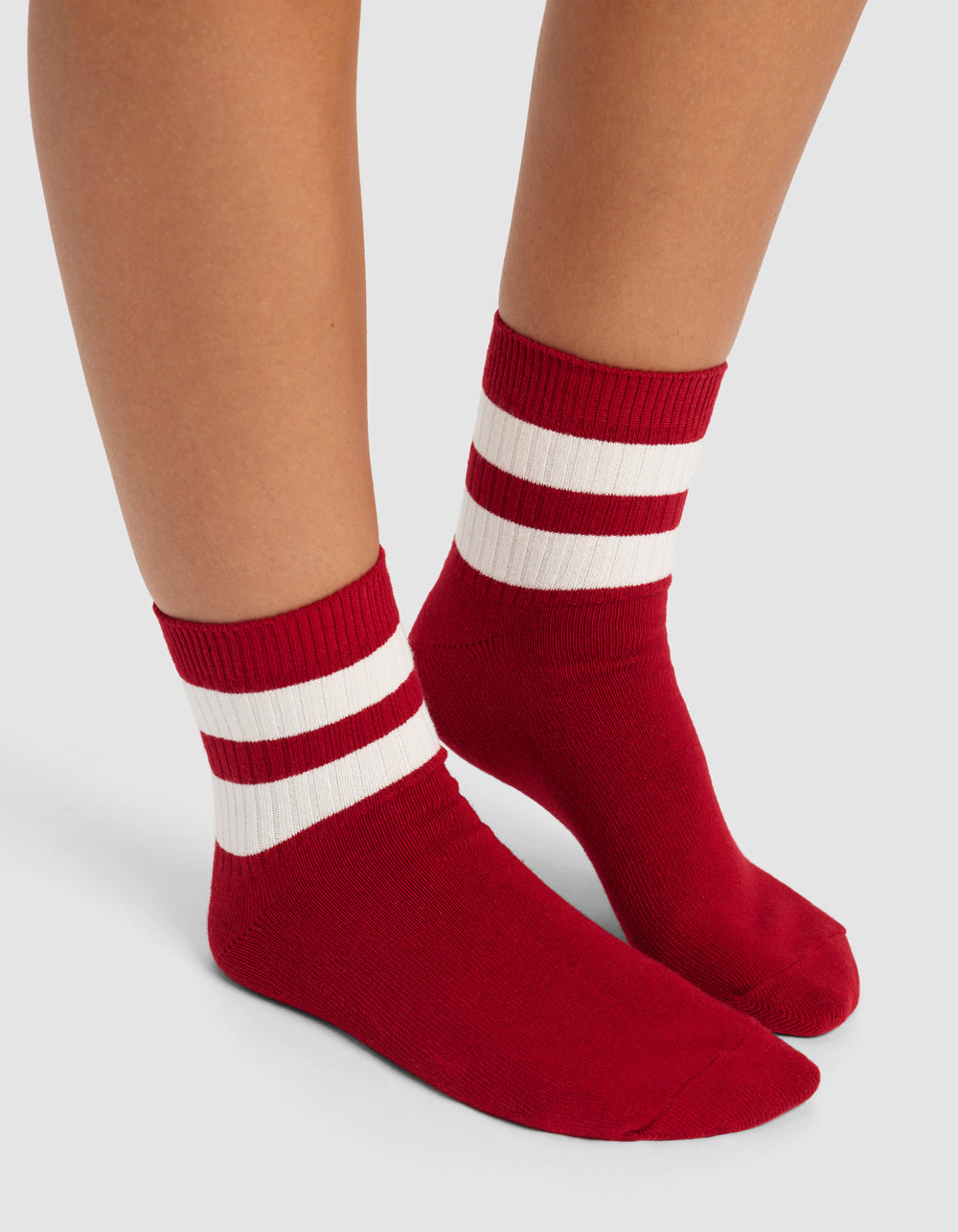 Two feet wearing Cozy Earth's Women's Sadie Sock, featuring red crew style with two white ankle stripes, shown against a light gray background.