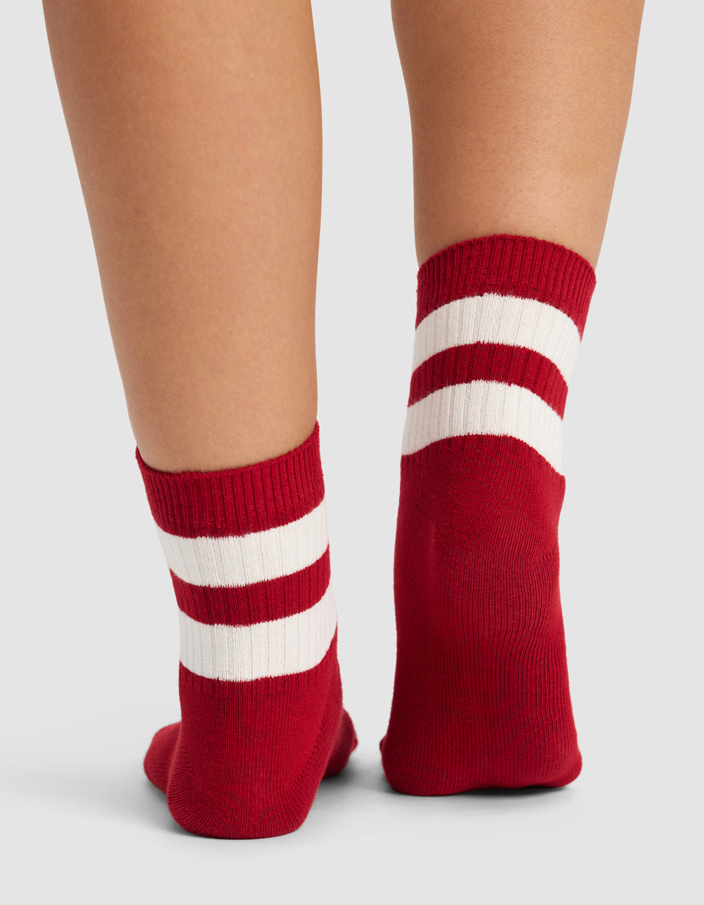 A close-up of two legs wearing Cozy Earth Women's Sadie Socks in red, featuring two white stripes near the top, shown against a plain light gray background.