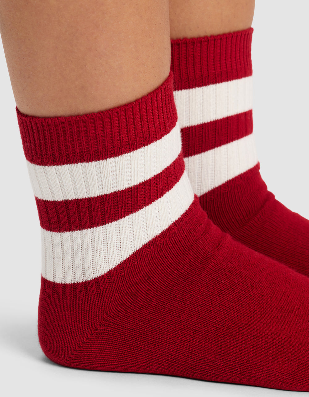 Close-up of a person wearing Cozy Earth's Women's Sadie Sock in red with two thick white stripes near the top, standing on a light gray surface.|Color:Crimson/Bone