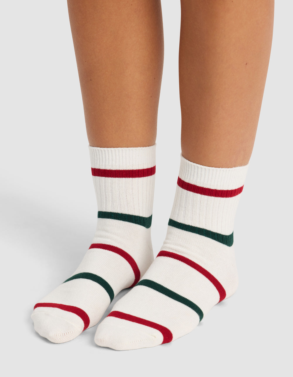 A pair of feet wearing Cozy Earth's Women's Sadie Sock—white crew socks with red and dark green stripes—stand on a light background.