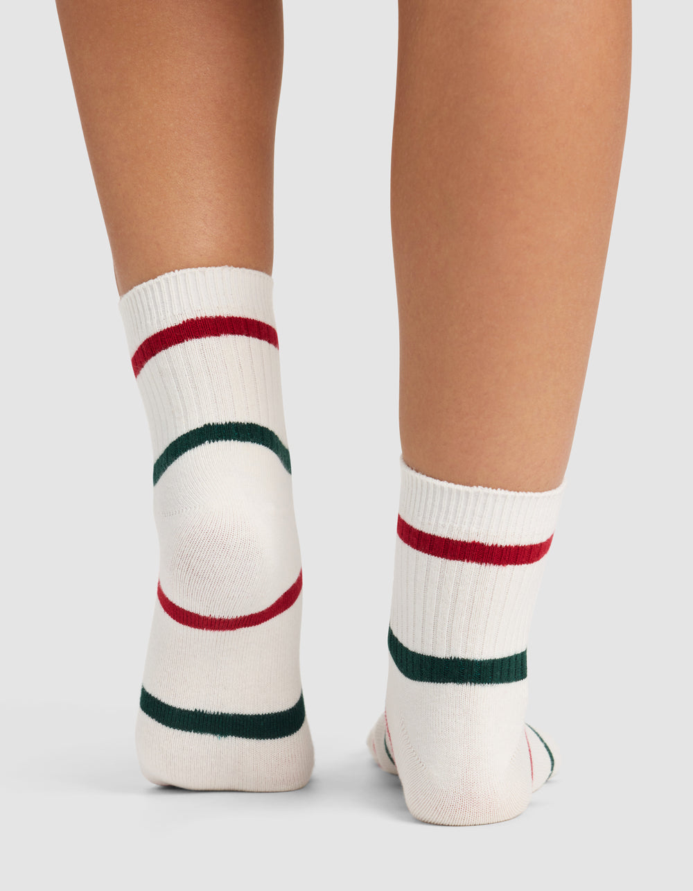 A close-up of two legs wearing Cozy Earth Women's Sadie Socks—white with red and green stripes—standing on a light surface. 