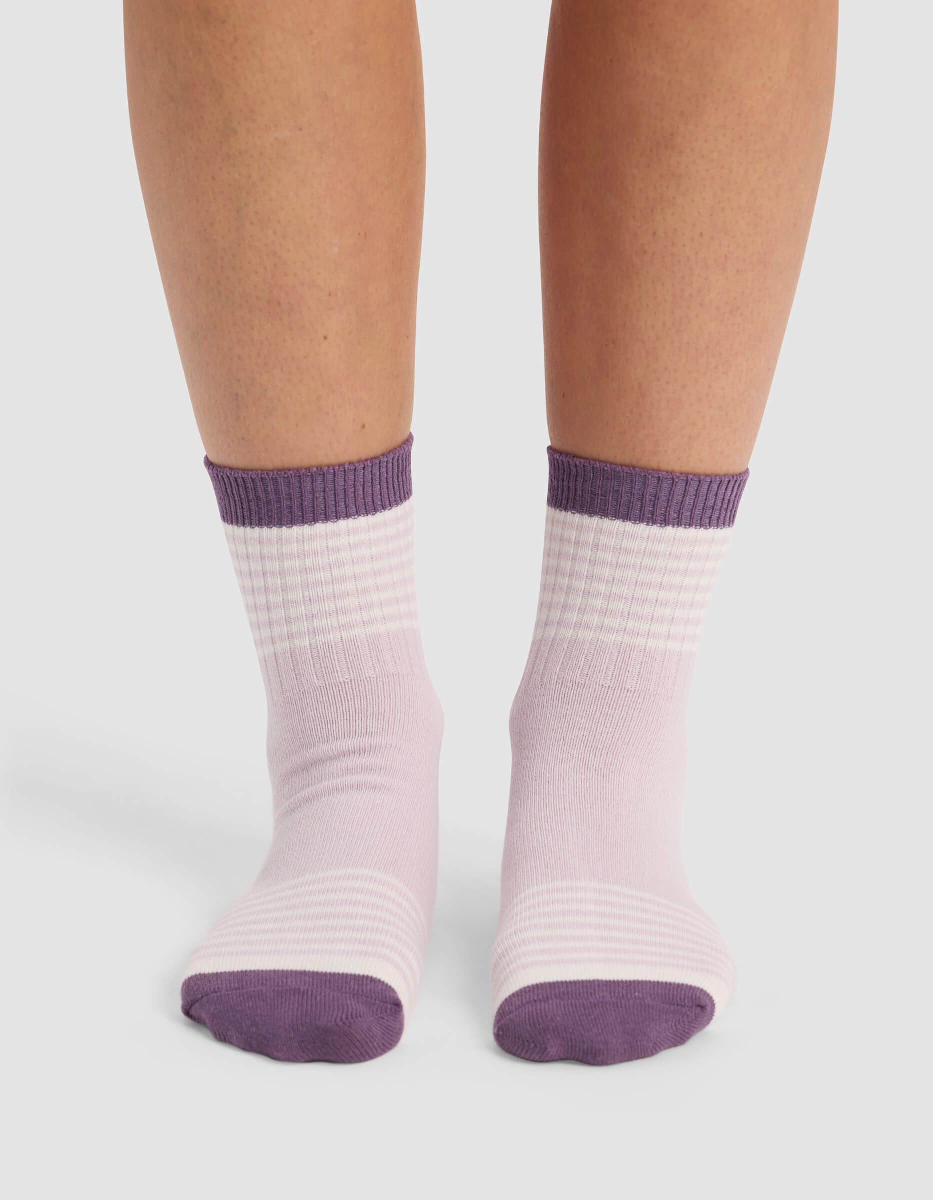 A pair of feet wearing Cozy Earth Women's Sadie Socks in light purple with darker purple toes, heels, and cuffs, standing on a white surface.