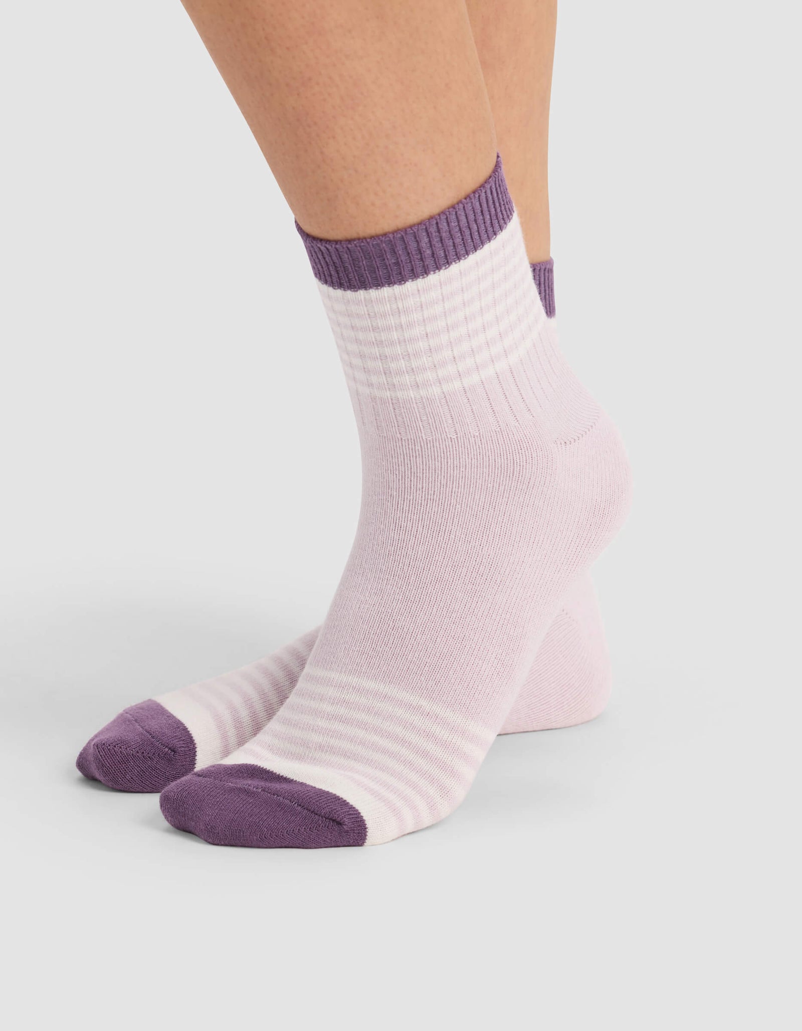 A person wearing Cozy Earth's Women's Sadie Sock in pastel pink with purple toes, heels, and cuffs stands on a light gray surface.