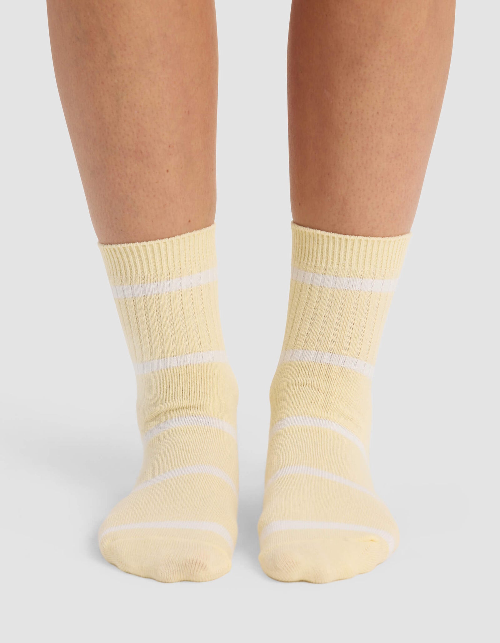 A person wearing Cozy Earth Women's Sadie Socks in yellow with white horizontal stripes stands on a light-colored surface; only their lower legs and feet are visible.