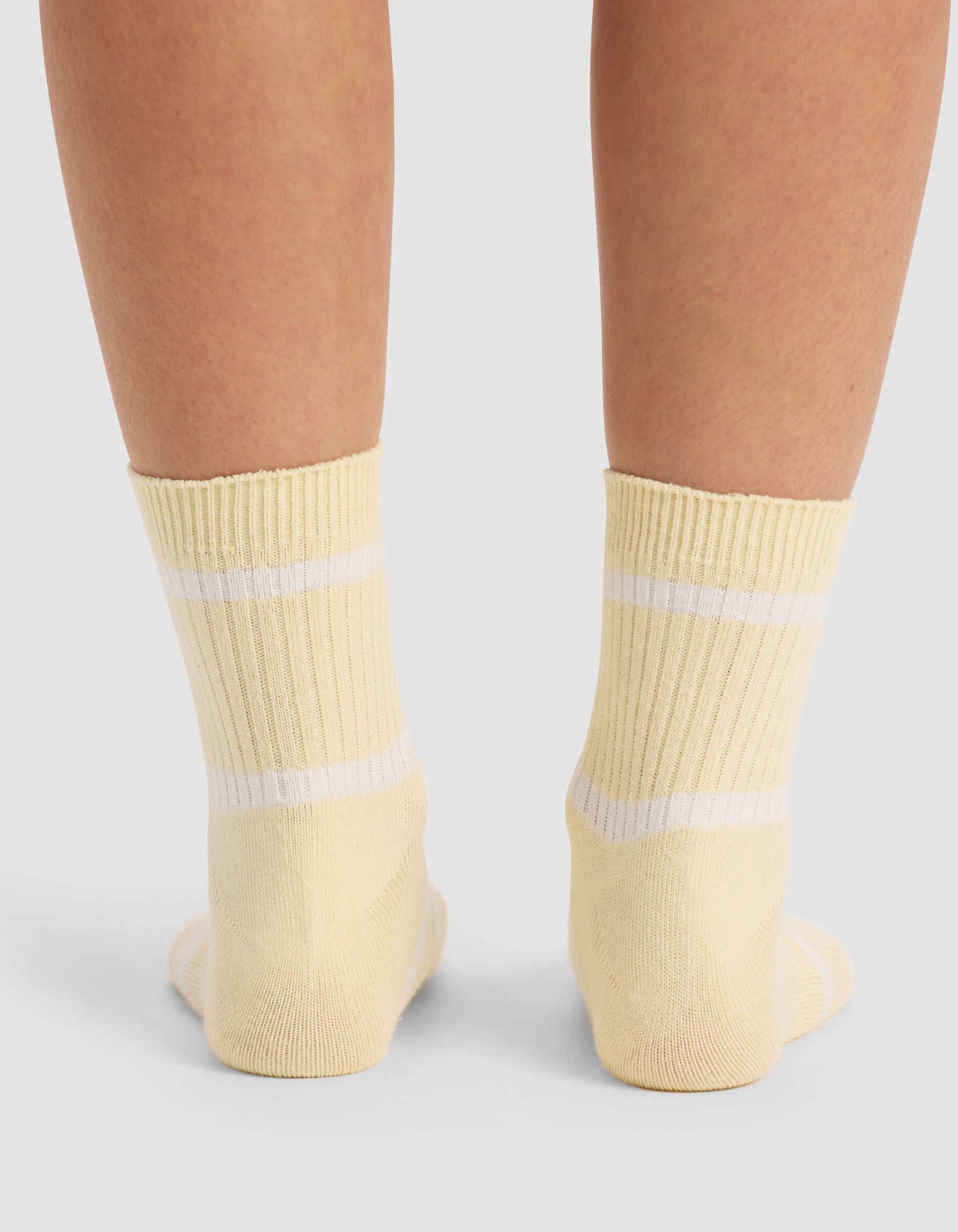A close-up of two feet wearing Cozy Earth Women's Sadie Socks in yellow with white stripes, standing on a light-colored surface.
