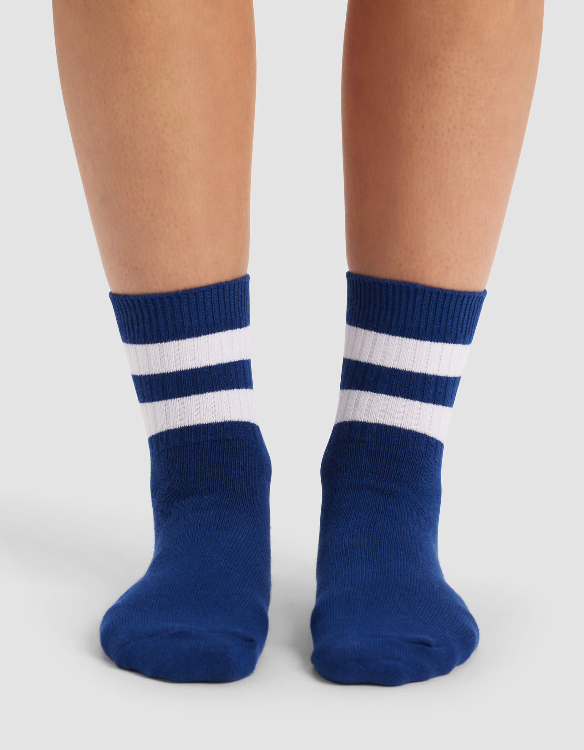 A person wears Cozy Earth's Women's Sadie Sock—blue with two white horizontal stripes near the top—while standing on a light surface.