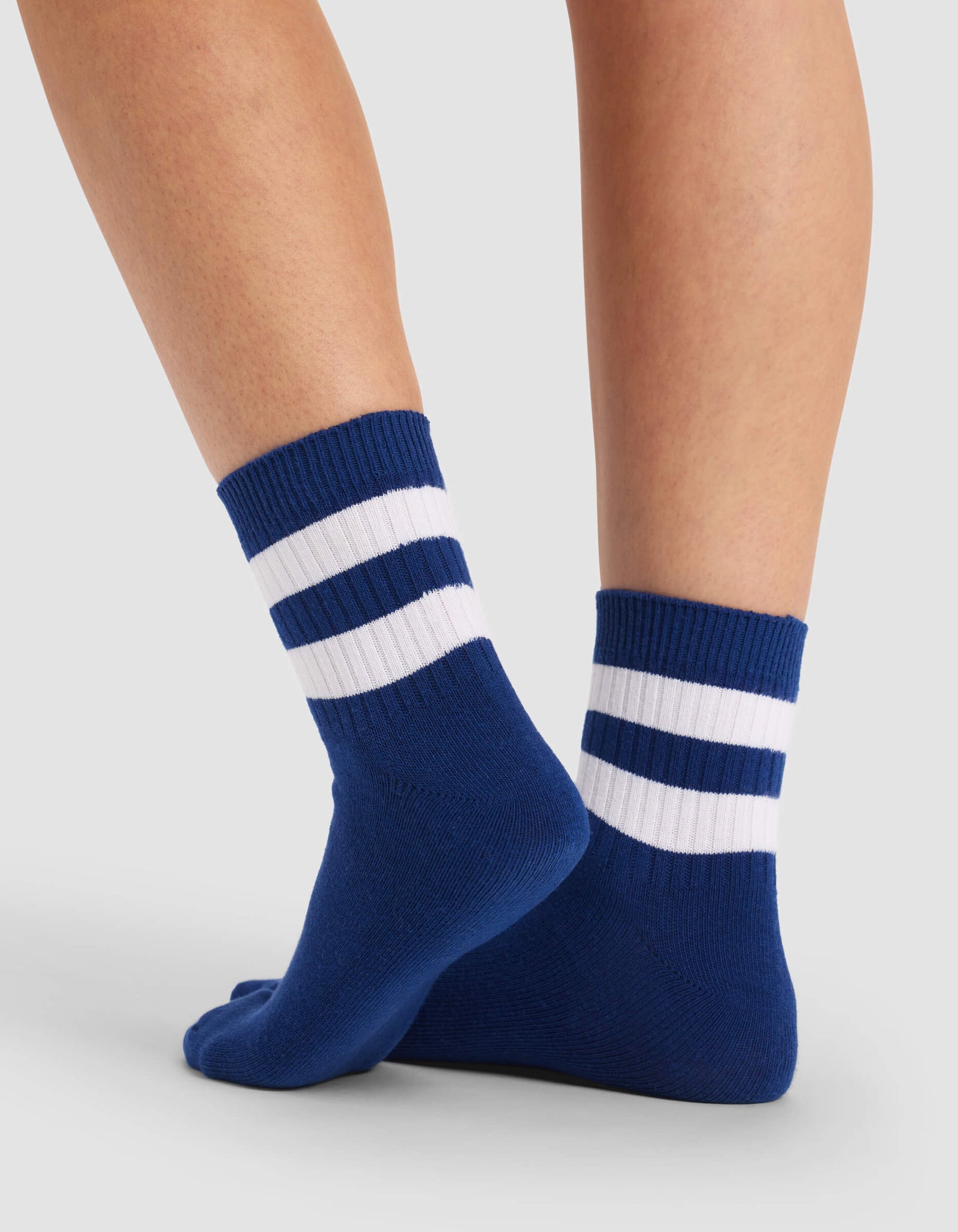 A pair of feet wearing Cozy Earth's Women's Sadie Socks in blue with two white stripes near the top, standing on a light gray surface.