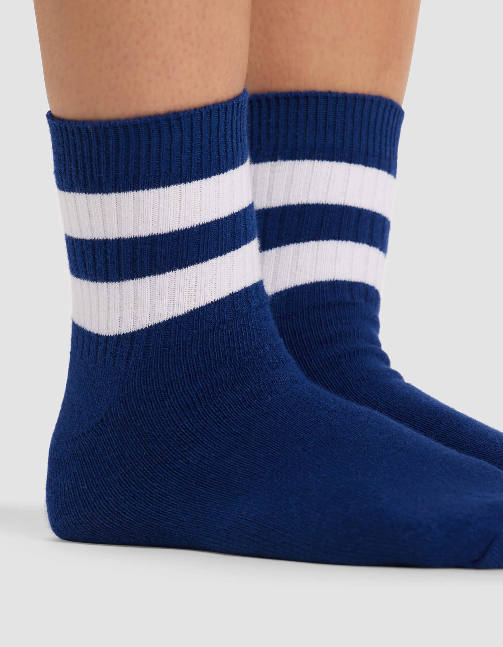 Close-up of two feet wearing Cozy Earth Women's Sadie Sock in blue with two white stripes near the top, standing on a light surface.