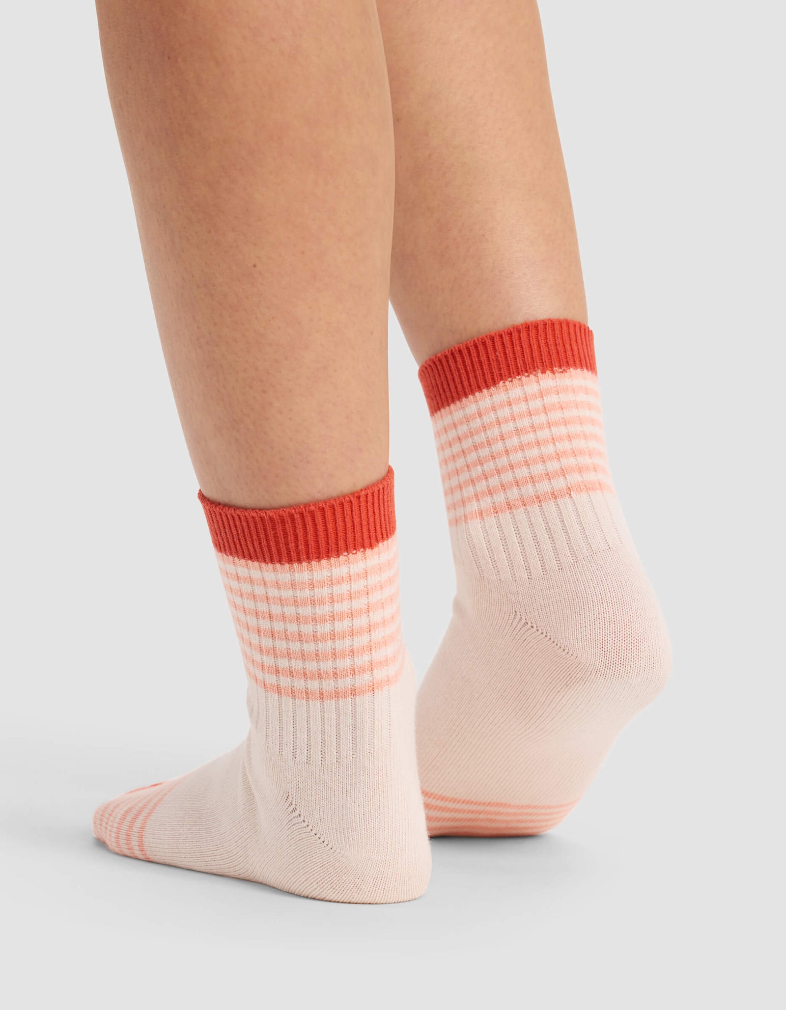 A person wears Cozy Earth Women's Sadie Socks—pale pink with red stripes and thick red cuffs—standing feet apart on a light gray surface, toes pointing down.