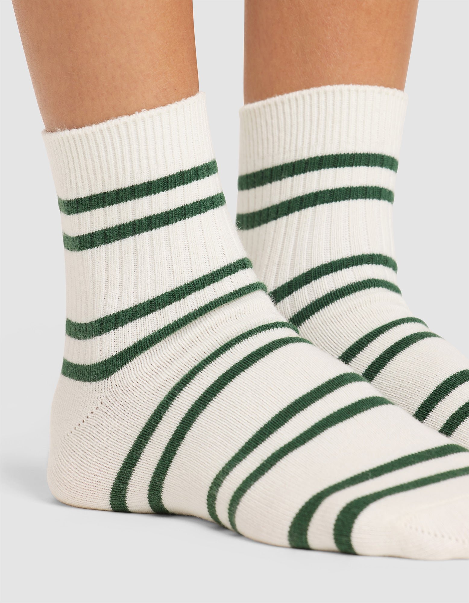 A close-up of two feet wearing Cozy Earth's Women's Sadie Sock, featuring white ribbed fabric with green horizontal stripes, set against a neutral background. 