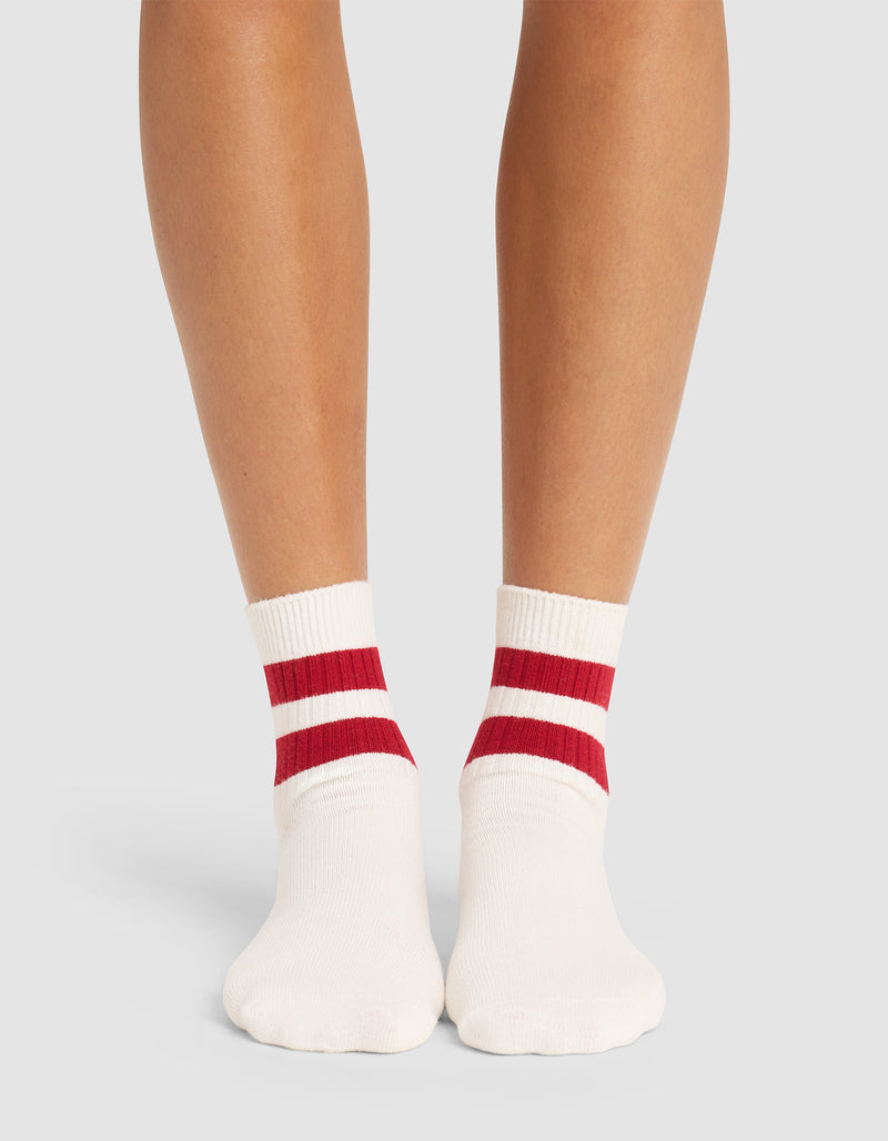 A person wears Cozy Earth's Women's Sadie Sock—white with red and white ankle stripes—standing barefoot and photographed from behind against a plain light background.