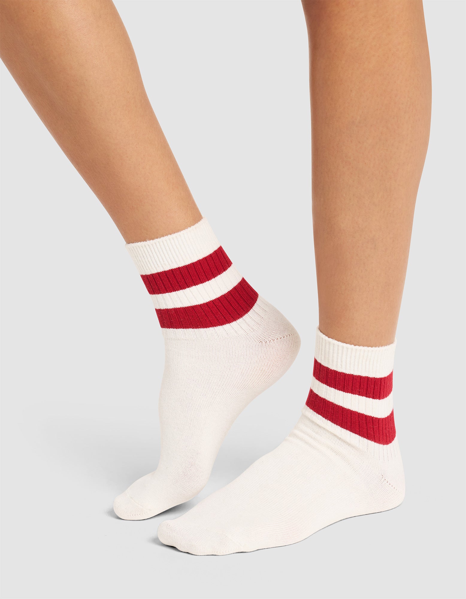 Two legs wearing Cozy Earth's Women's Sadie Sock—white ribbed socks with two thick red stripes at the ankles—stand on a light grey background.  