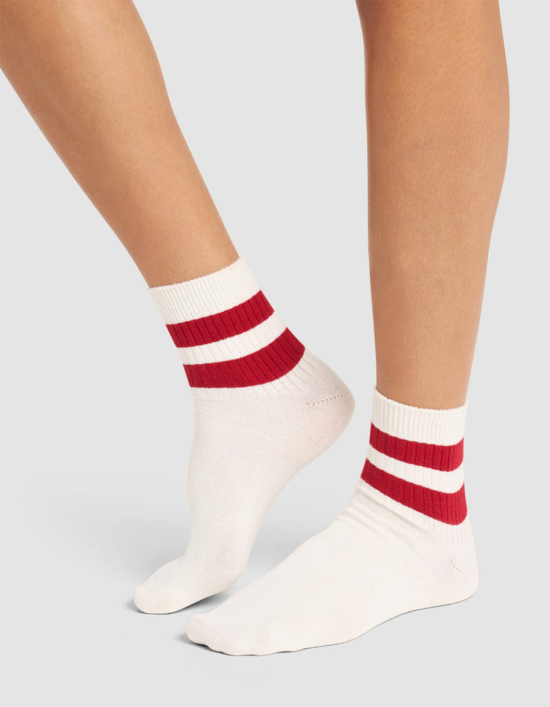 Two legs wearing Cozy Earth's Women's Sadie Sock—white ribbed socks with two thick red stripes at the ankles—stand on a light grey background.